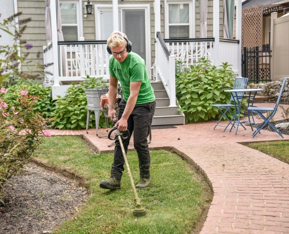 A landscaper edging a bed beside a house with a brick walkway