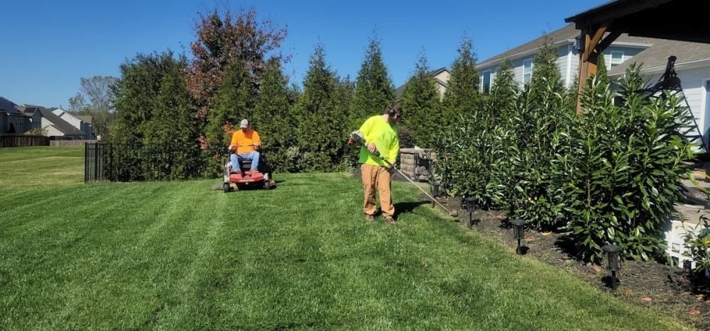 Two groundskeepers mowing and trimming a large striped lawn
